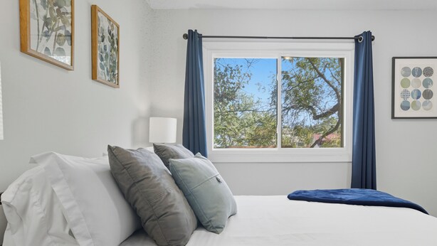 A bedroom with a bed, pillows, a window with curtains, and framed pictures on the wall. - Cozy 2BR / Close to Mayo Clinic / Full Kitchen & Private Backyard (Rochester)