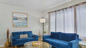 A living room with two blue sofas, a glass coffee table, a lamp, and a painting on the wall. - Cozy 2BR / Close to Mayo Clinic / Full Kitchen & Private Backyard (Rochester)