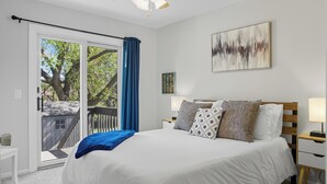 Une chambre avec un grand lit, un ventilateur de plafond, une porte-fenêtre coulissante donnant sur un balcon et un tableau accroché au mur.
