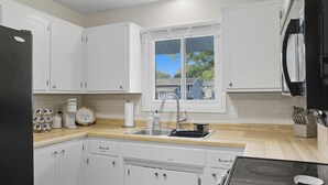 A kitchen with white cabinets, a stainless steel sink, a black refrigerator, and a window with a view of houses. - Cozy 2BR / Close to Mayo Clinic / Full Kitchen & Private Backyard (Rochester)