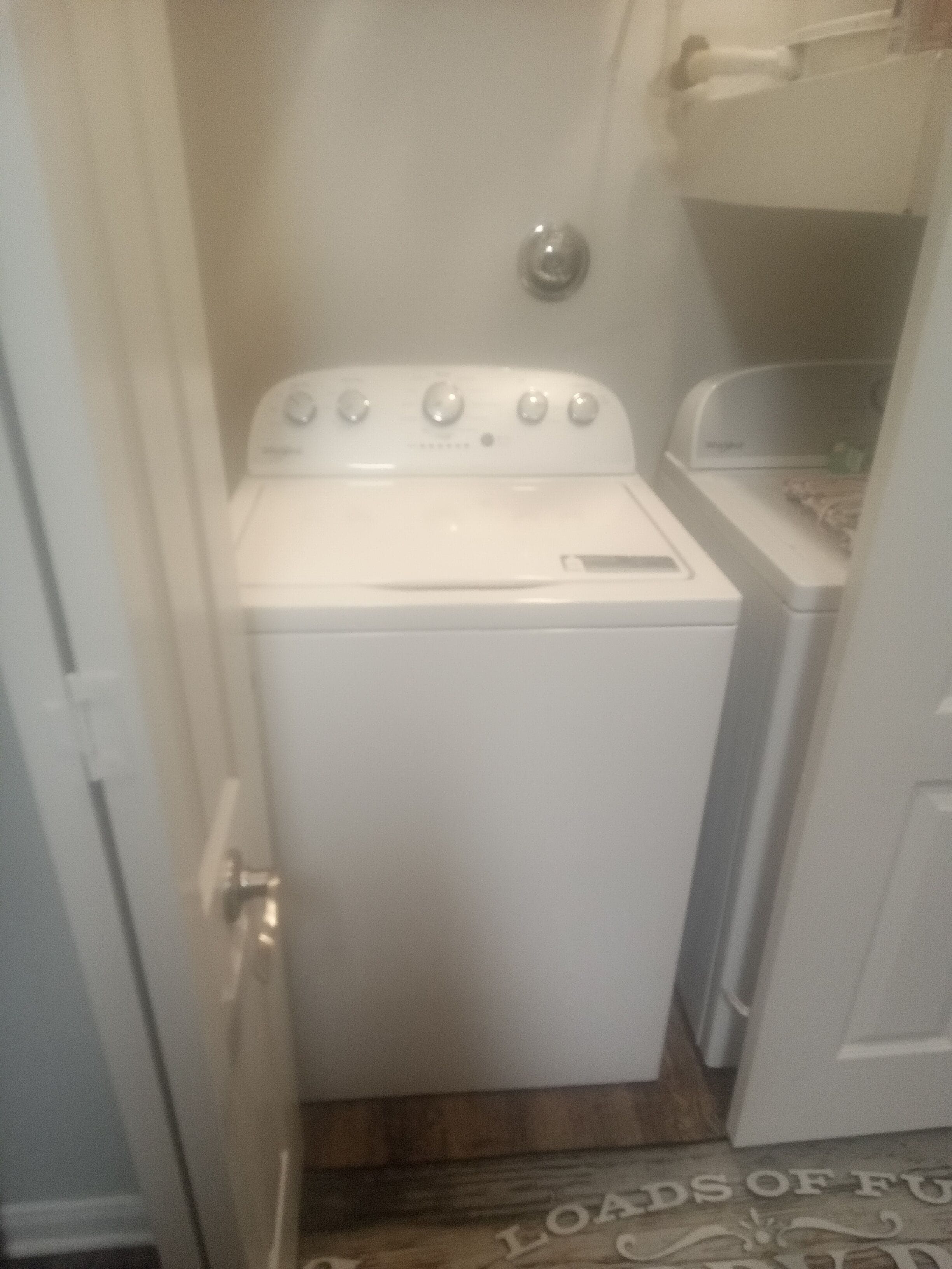 A compact laundry room with a front-loading washer and dryer, a wooden floor, and a door with a handle.