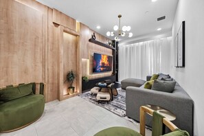 Uma sala de estar moderna com televisão de tela plana, um sofá cinza, uma poltrona verde e um painel de parede em madeira.