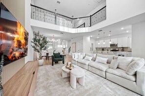 A spacious living room with a large flat-screen TV, a sectional sofa, and a staircase leading to an upper level. - 5BR house sleeps 14 with pool table (Kissimmee)