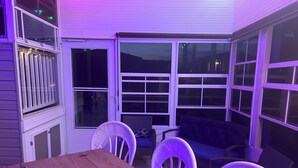 A patio area with a wooden table and white chairs, a wicker sofa, and a window with a view of the night sky. - 2-bedroom 2bath mobile home in lovely Alligator Park Punta Gorda FL with AC (Punta Gorda)