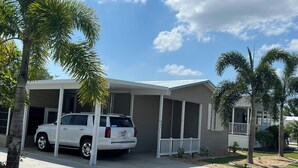 A single-story house with a covered porch, a driveway, and a parked SUV. - 2-bedroom 2bath mobile home in lovely Alligator Park Punta Gorda FL with AC (Punta Gorda)