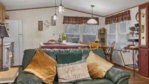 A cozy living room with a green leather sofa, a dining table with chairs, and a kitchen area with a refrigerator and a sink. - Lake Limestone Getaway w/ Firepit (Groesbeck)