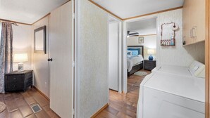 A room with a bed, bedside table, lamp, and a white washing machine. - Lake Limestone Getaway w/ Firepit (Groesbeck)
