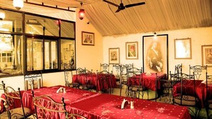 Un comedor con mesas cubiertas de manteles rojos, sillas de metal, ventiladores de techo y cuadros en las paredes.