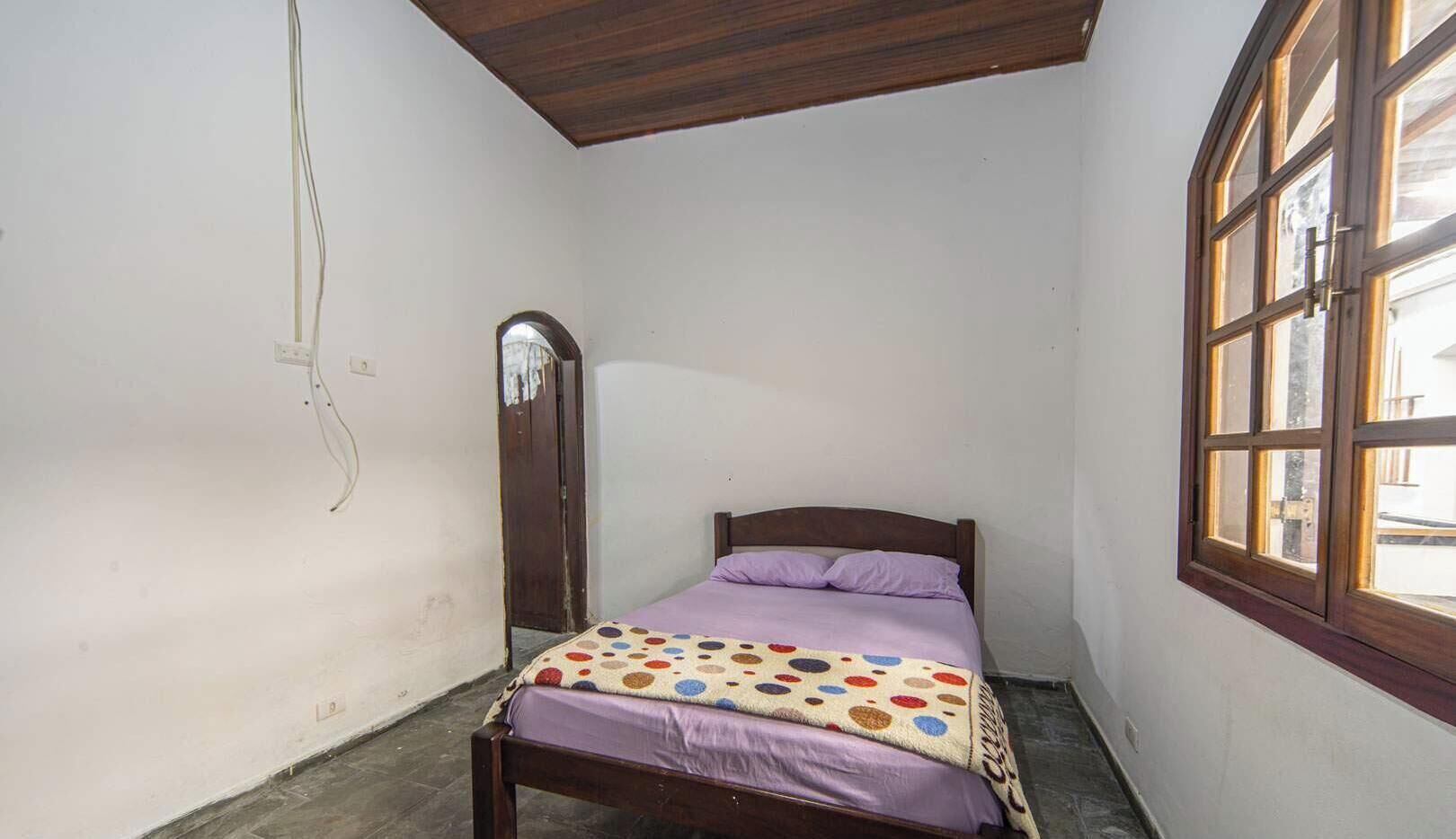 Ein kleines Zimmer mit einem Einzelbett, Holzboden, einem Fenster mit Holzrahmen und einer Tür mit Spiegel.
