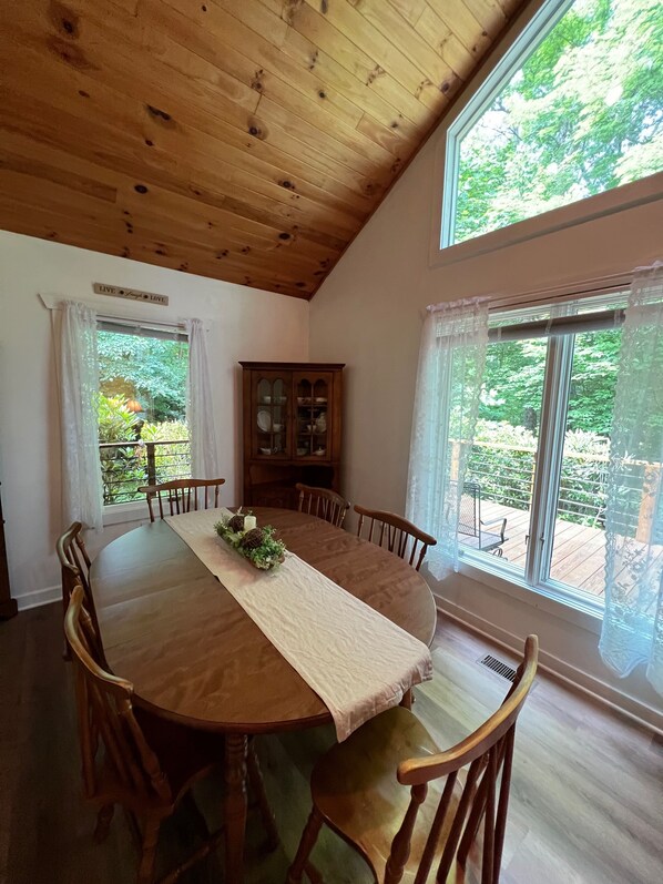 Ein Esszimmer mit Holztisch, Stühlen, einem Schrank und großen Fenstern mit Vorhängen.