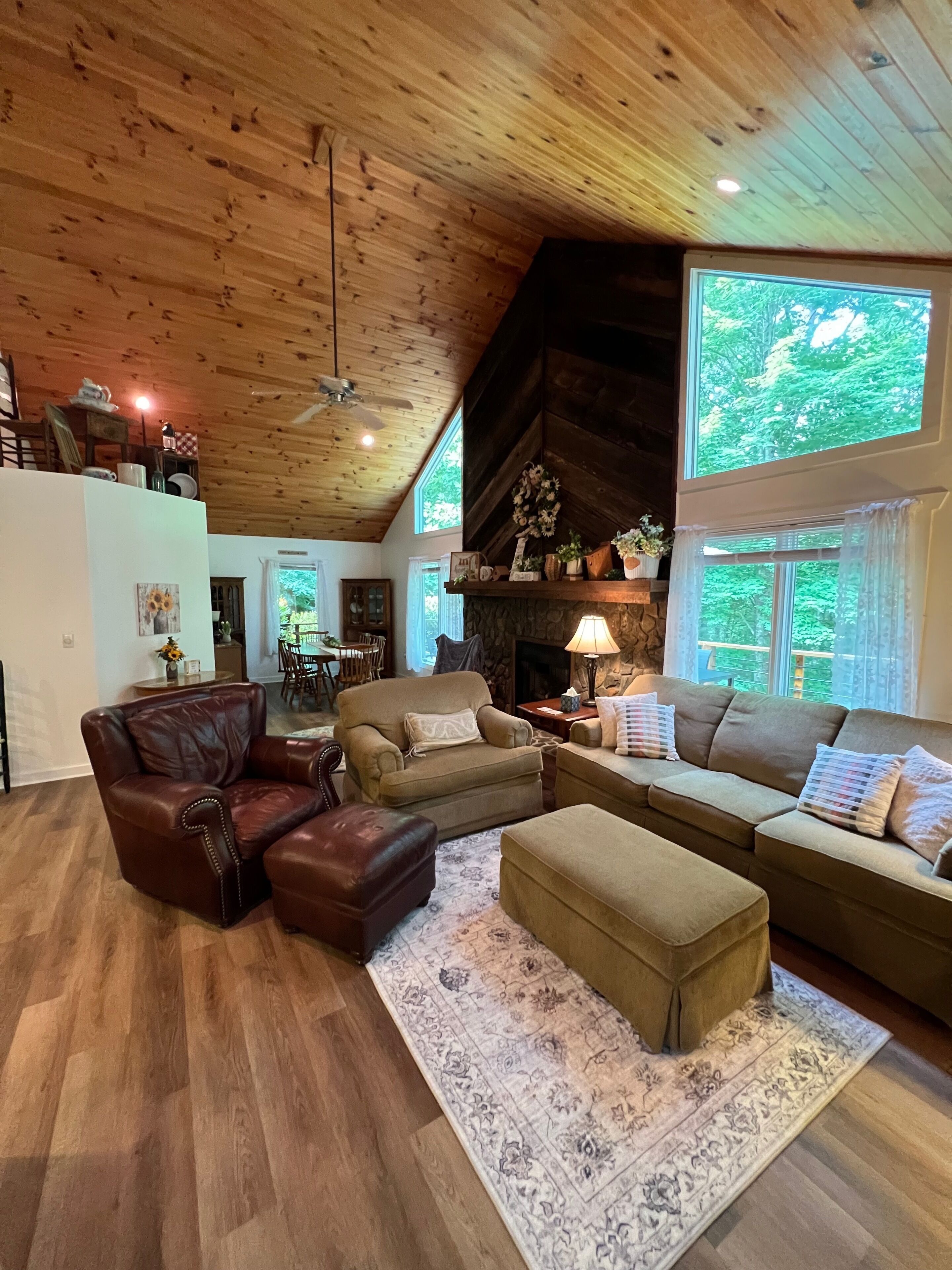 A cozy living room with a fireplace, leather furniture, and a large window overlooking greenery.