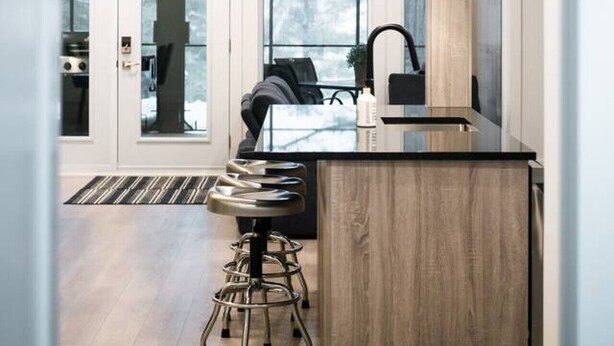 A modern kitchen with a central island, bar stools, and a pendant light. - Lynx Spa et confort à Orford (Orford)