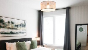 A modern bedroom with a large bed, a bedside table, a lamp, a mirror, and a window with curtains. - Lynx Spa et confort à Orford (Orford)