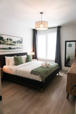 Un dormitorio moderno con una cama grande, una mesita de noche, una lámpara, un espejo y una ventana con cortinas.