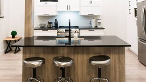 A modern kitchen with white cabinets, a central island with bar stools, and pendant lighting. - Lynx Spa et confort à Orford (Orford)