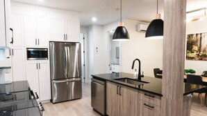 A modern kitchen with stainless steel appliances, a black countertop, and wooden cabinets. - Lynx Spa et confort à Orford (Orford)