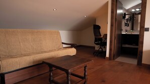 A room with a sofa, a wooden coffee table, and a desk with a chair. There is a doorway leading to another room. - HOTEL POSADA LAS RETAJAS (Medinaceli)