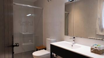 A modern bathroom with a glass shower enclosure, a white toilet, a sink with a black countertop, and a mirror above the sink.
