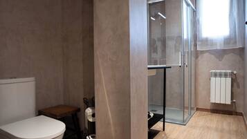 A modern bathroom with a toilet, a small wooden table, a glass shower enclosure, and a radiator.