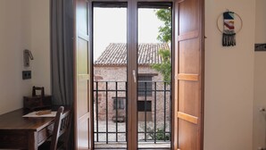 A room with a wooden desk, a chair, and a view through a glass door to an outdoor area with a tiled roof and a stone wall. - HOTEL POSADA LAS RETAJAS (Medinaceli)