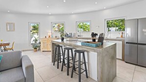 A modern kitchen with a central island, bar stools, a refrigerator, and a dining area with a sofa and table. - NEW 3BR Villa Salina Cerca | Close to Eduardo’s (Noord)