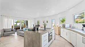 A modern kitchen with a central island, white cabinetry, and a large window overlooking a garden. - NEW 3BR Villa Salina Cerca | Close to Eduardo’s (Noord)