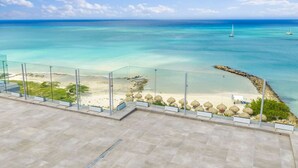 Ein Balkon mit freiem Blick auf Strand und Meer, ausgestattet mit einem Glasgeländer und einem Steinboden.