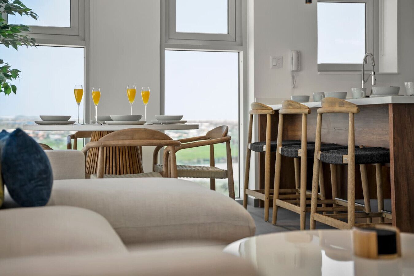 A modern living room with a sofa, a dining table with chairs, and a kitchen area with bar stools.