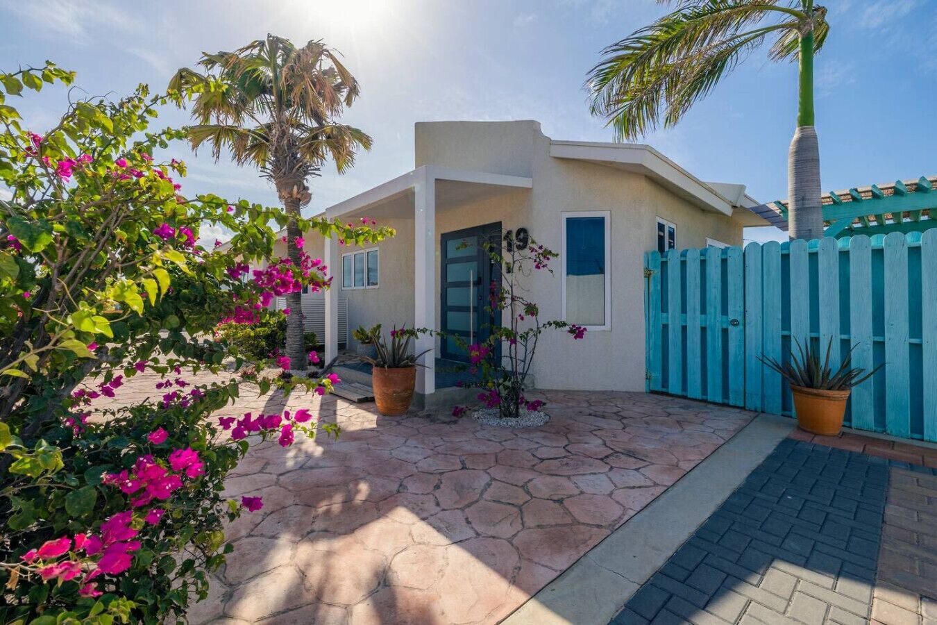 A house with a stone patio, a blue fence, and bougainvillea flowers.