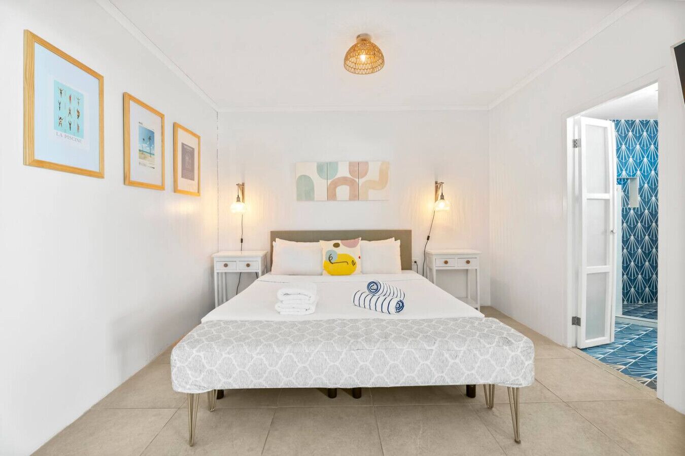 A hotel room with a bed, two bedside tables, a wall-mounted lamp, and framed pictures on the wall.