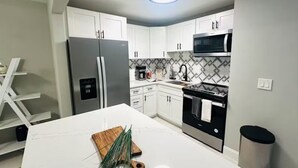 Eine moderne Küche mit weißen Schränken, einem Edelstahl-Kühlschrank, einer Mikrowelle und einer Marmorarbeitsplatte.