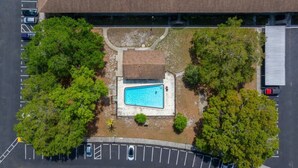 Eine Vogelperspektive zeigt ein Anwesen mit Swimmingpool, Parkplatz und umliegender Bepflanzung.