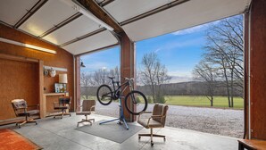 Een ruime kamer met een groot raam, een op een standaard geplaatste fiets en een zithoek met stoelen en een bank.
