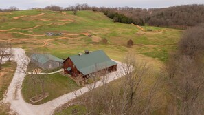 A large barn with a green roof, surrounded by a dirt path and a grassy field. - Coyote Cabin • Hot Tub + Trails at Two Rivers (Highlandville)