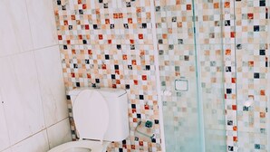 Un baño con suelo de baldosas, inodoro blanco y zona de ducha con puerta de cristal.