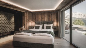 A modern bedroom with a large bed, wooden panel walls, and a view of mountains through a large window. - Chalet Lavinia by My Villa Collection (Selva Gardena)