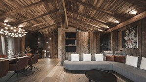 A modern living room with a wooden ceiling, a grey sofa, and a dining area with a table and chairs. - Chalet Lavinia by My Villa Collection (Selva Gardena)