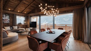 A spacious room with a large wooden table, comfortable seating, a television, and a view of a snowy mountain landscape. - Chalet Lavinia by My Villa Collection (Selva Gardena)