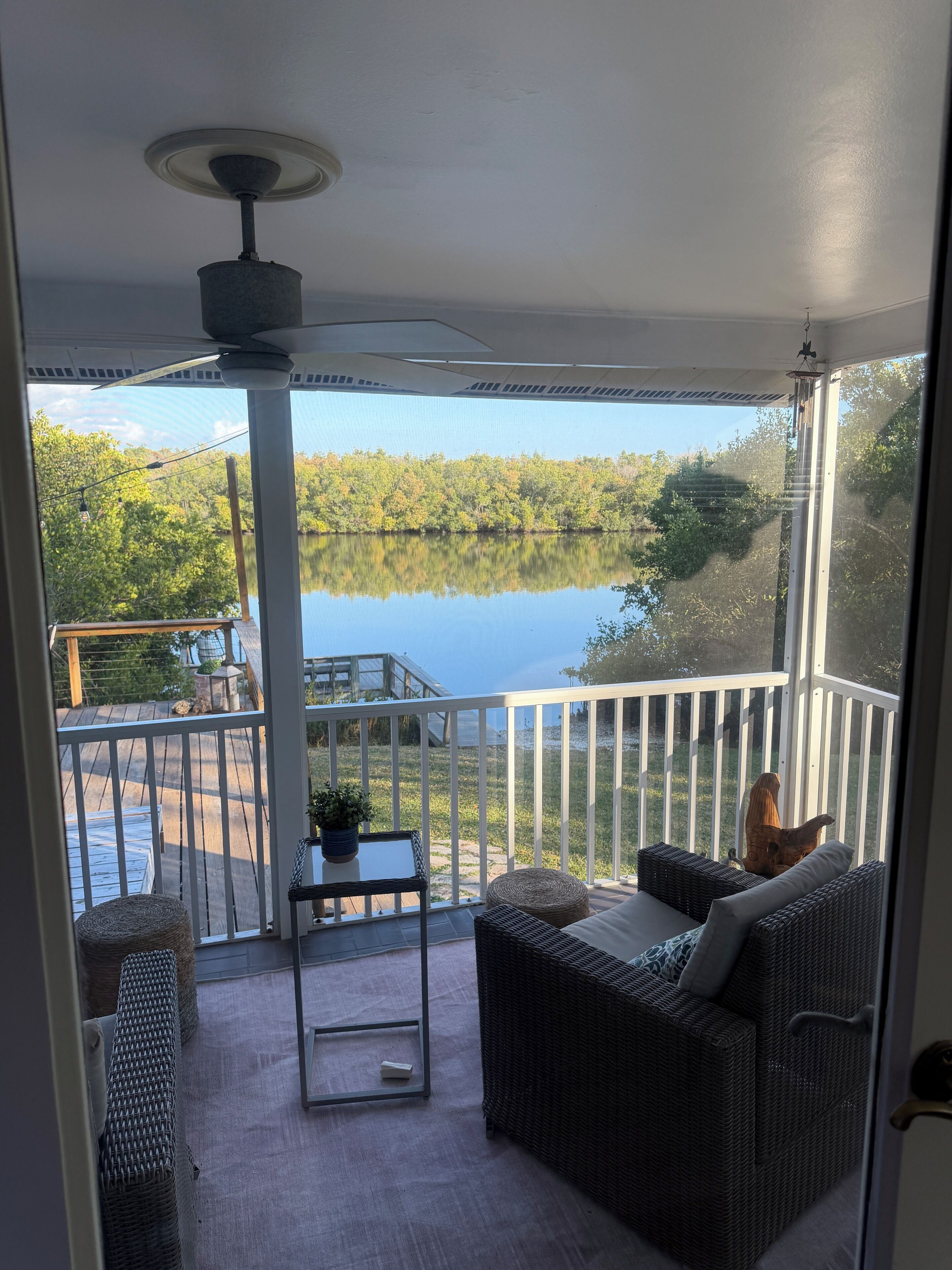 A balcony with wicker furniture, a small table, and a view of a lake surrounded by trees.