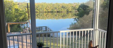 A balcony with wicker furniture, a small table, and a view of a lake surrounded by trees.