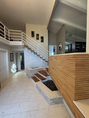 Interior moderno com escada para um mezanino, área de cozinha e espaço de estar com um banco de madeira.