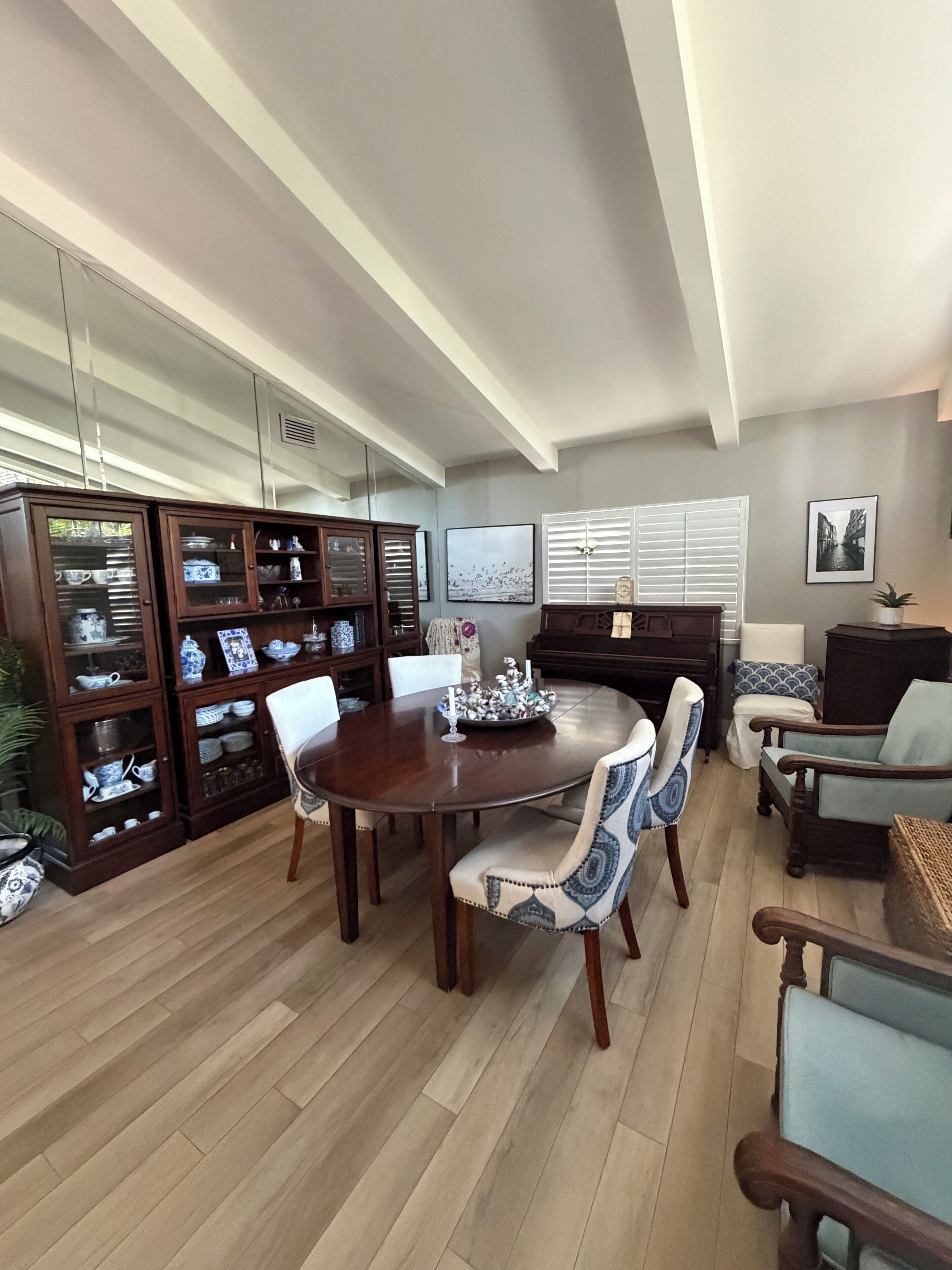 A dining area with a wooden table and chairs, a piano, and a cabinet with glass doors.