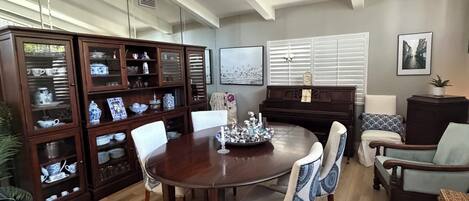 A dining area with a wooden table and chairs, a piano, and a cabinet with glass doors.