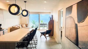 Une cuisine moderne avec un grand îlot central, des chaises noires et une grande fenêtre donnant sur un balcon.