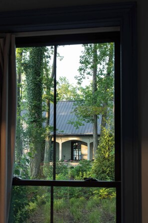 En vy genom ett fönster i ett hus som omges av träd och grönska.