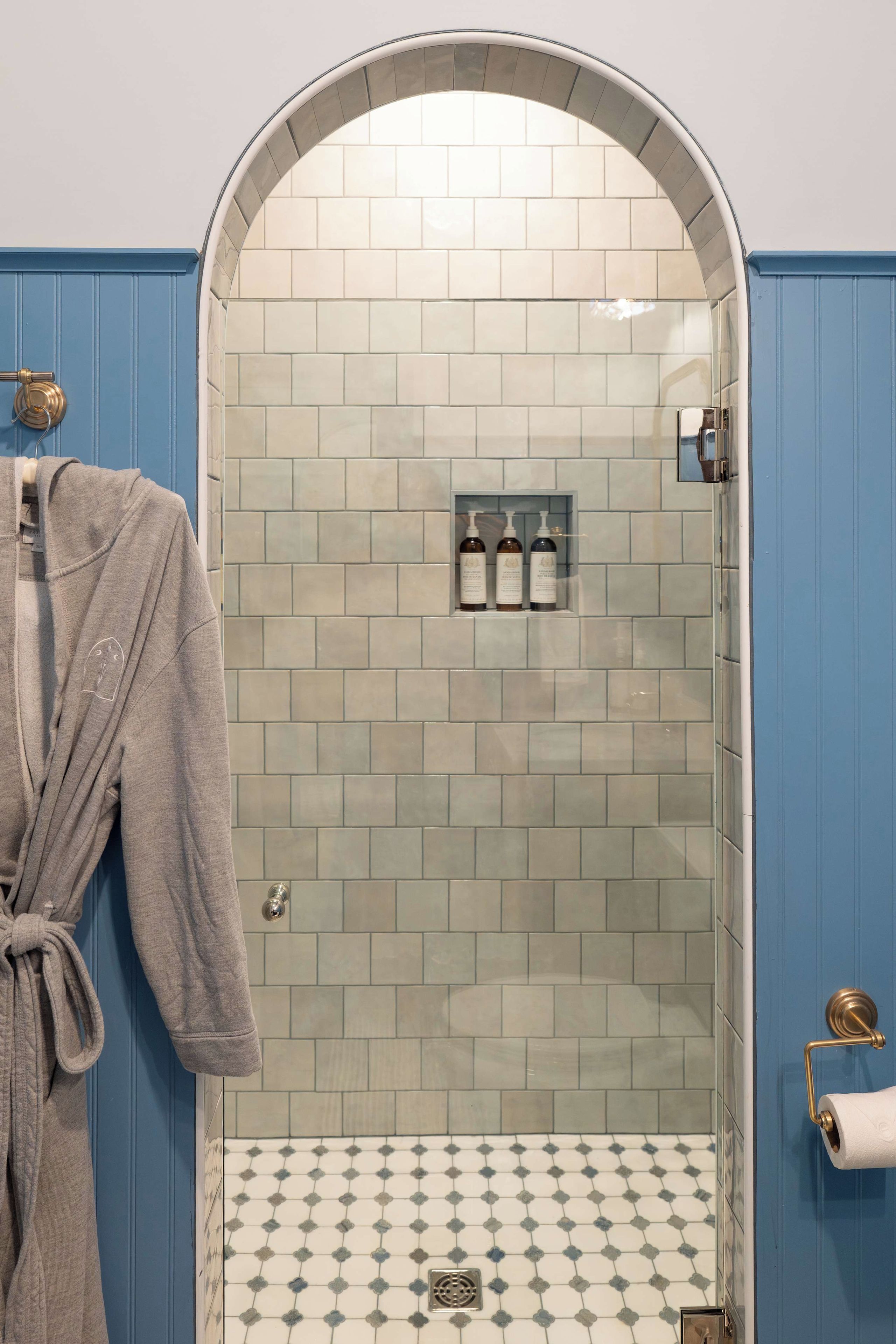 A bathroom with a shower area, a towel rack, and a tiled floor.