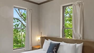 A hotel room with a large bed, two windows with curtains, a bedside table with a lamp, and a hanging light fixture.