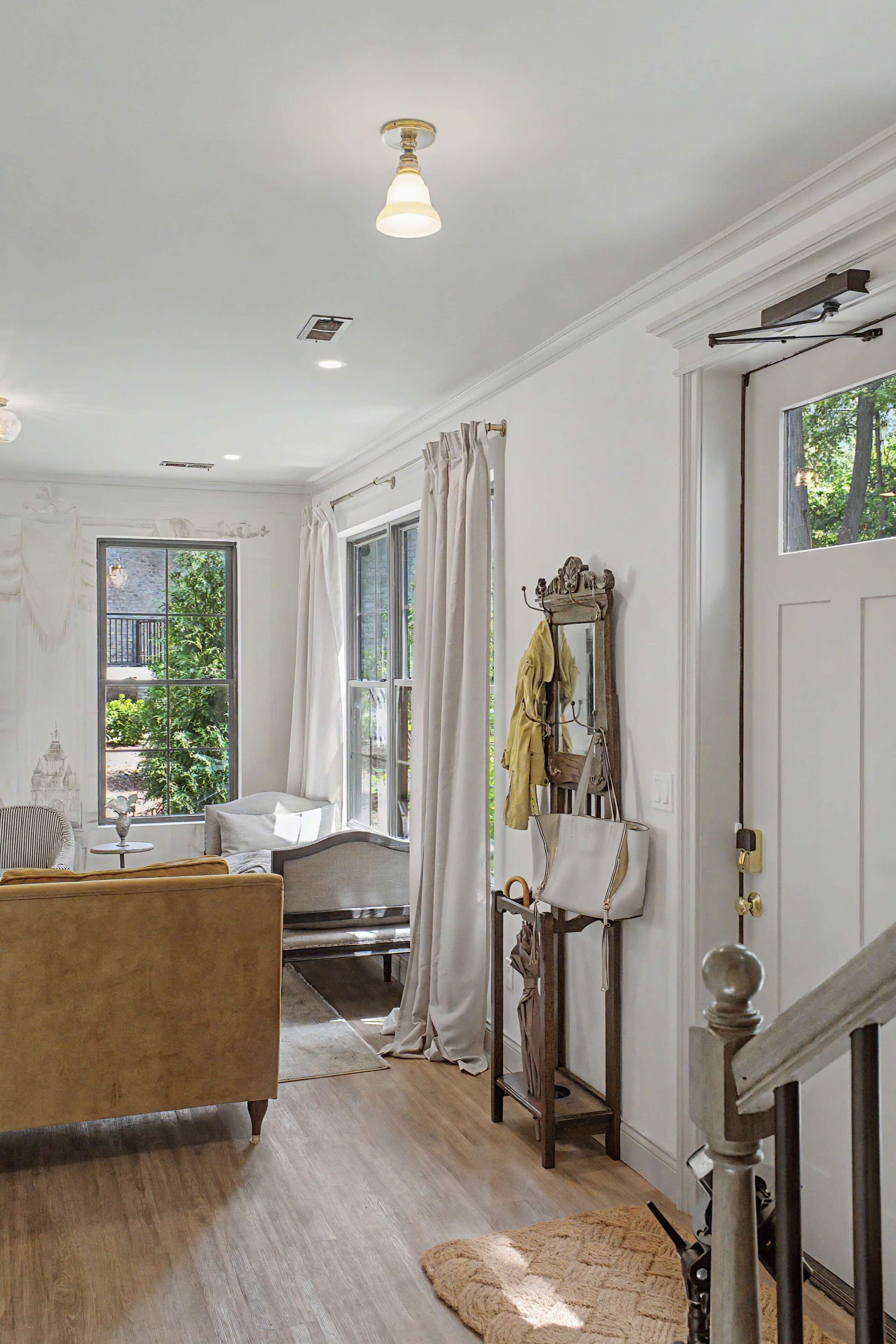 Une pièce comprenant un lit, une table avec un miroir, une fenêtre avec des rideaux et une porte avec un porte-manteau.