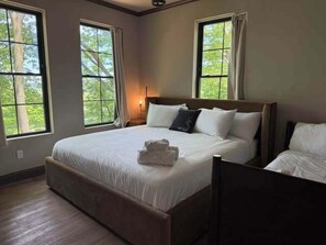 Une chambre avec un grand lit, deux fenêtres, une table de chevet et un plancher en bois.