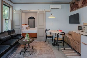 Habitación de hotel compacta con sofá, cama, zona de comedor con sillas, pequeña mesa, microondas y televisor en la pared.